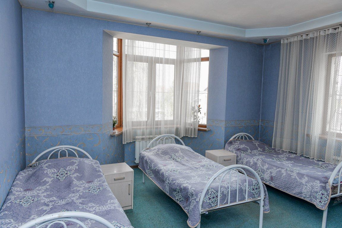 Трёхместная палата в голубых тонах: кровати вдоль стен, эркерное окно с занавесками