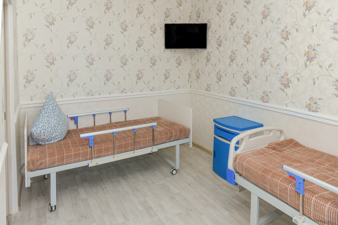 Двухместная палата: две функциональные кровати с боковыми ограждениями, тумбочка между ними, телевизор на стене
